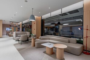 A modern lounge area with a sectional sofa, round tables, and a large window offering a view of the interior.