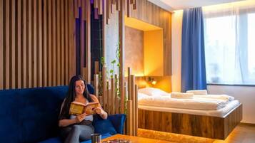 Ein Hotelzimmer mit einer Couch, einem kleinen Tisch mit einer Schale, einem Bett und einem Fenster mit Vorhängen.