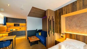 Ein modernes Hotelzimmer mit einer Wandpaneele aus Holz, einem Sofa, einem Bett und einer Küchenzeile.