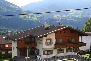Ein traditionelles Chalet mit Balkon, einem Schild mit der Aufschrift 'Gasthof' und einer Bergkulisse.