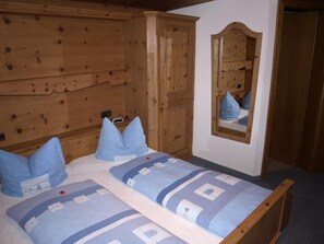 Ein Schlafzimmer mit Holzschrank, einem Bett mit blauer Bettwäsche und einem Spiegel an der Wand.