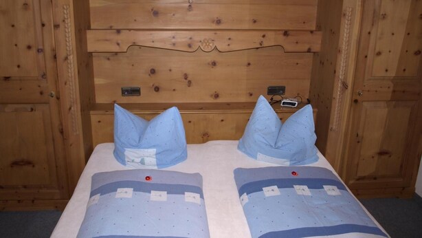 A wooden headboard with a built-in heater, two pillows, and a bed with a patterned bedspread. - Apartment “Gästehaus Christoph” with Mountain View, Balcony and Wi-Fi (Ried im Zillertal)