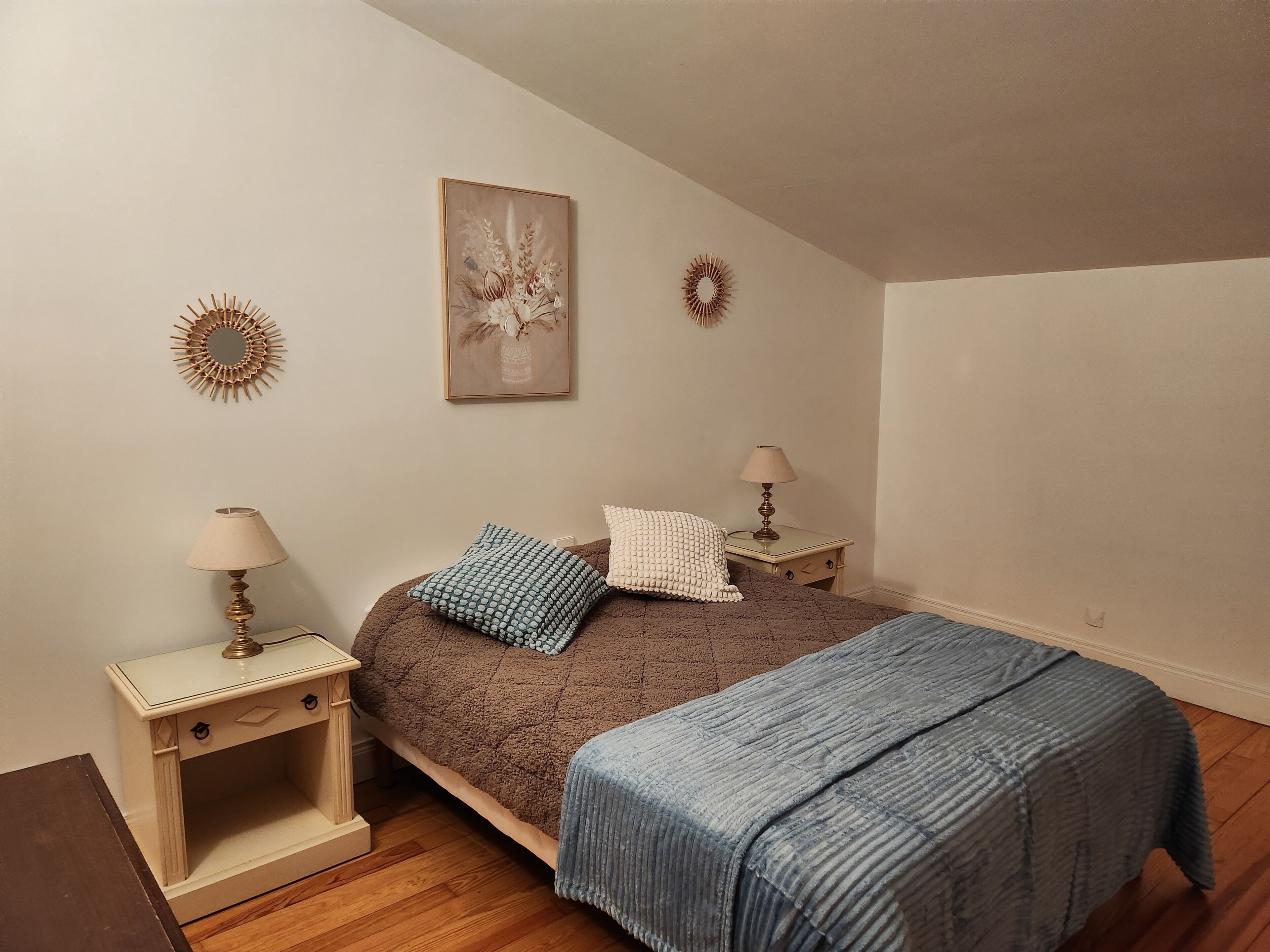 Une chambre à coucher comprenant un lit, deux tables de chevet, une lampe, un miroir décoratif et une œuvre d’art accrochée au mur.