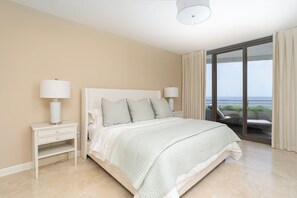 Ein Schlafzimmer mit einem Bett, Nachttischlampen, einem Nachttisch und Blick auf das Meer durch ein großes Fenster.