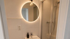 A modern bathroom with a glass-enclosed shower, a white sink with a mirror above it, and a toilet. - Copy of To complete (Dormagen)