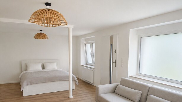 Ein Schlafzimmer mit einem Bett, einem Sofa, einem Fenster und einer Lampenschirm aus Rattan.