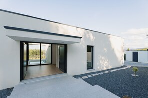 A modern building with a large glass door entrance, a small window, and a gravel pathway leading to the door. - Feel Discovery Douro Living Villa I (Paços de Gaiolo)