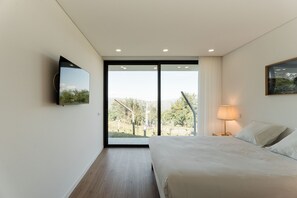 Ein modernes Hotelzimmer mit einem großen Bett, einem an der Wand befestigten Flachbildfernseher und einer Glasschiebetür zu einem Außenbereich.