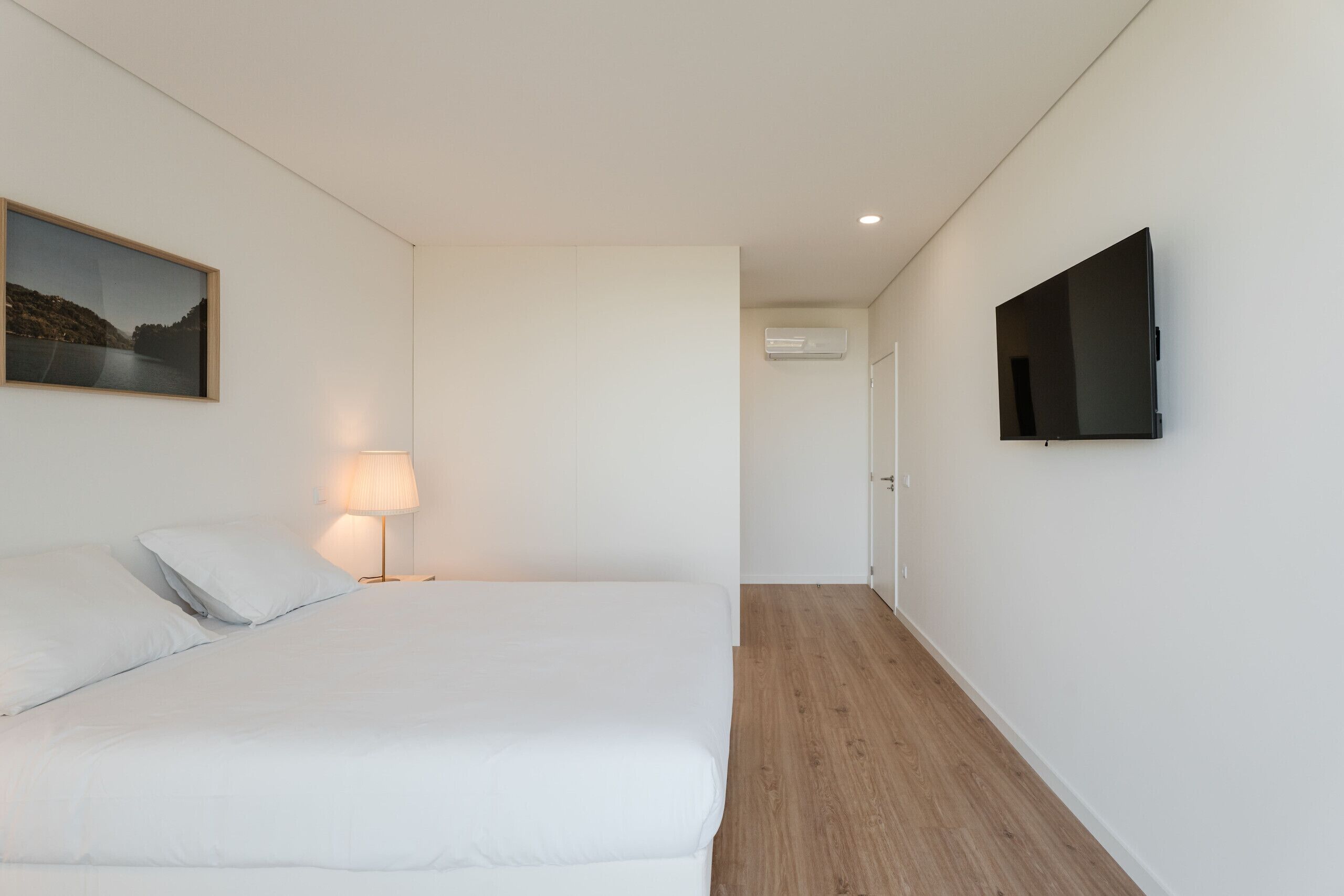 Een hotelkamer met een bed, een televisie, een schilderij en een airconditioner.