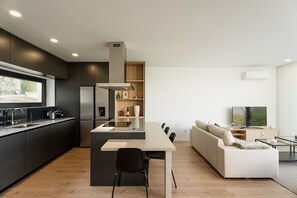 A modern kitchen with a central island, a dining area, a sofa, and a TV in a living room. - Feel Discovery Douro Living Villa I (Paços de Gaiolo)