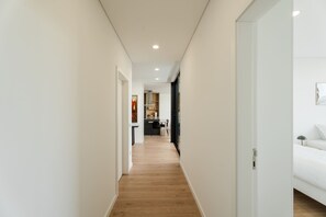 A narrow hallway with wooden flooring leading to a kitchen area with modern appliances and a dining table. - Feel Discovery Douro Living Villa I (Paços de Gaiolo)