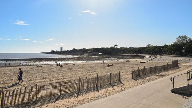 Ein Strand mit einer Holzzaun, einem Betonweg und blauem Himmel.