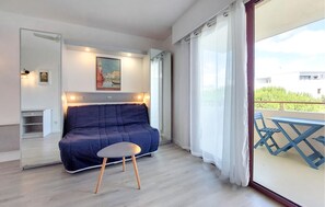 Ein Zimmer mit einem blauen Sofa, einem kleinen runden Tisch, einem Gemälde von Venedig und einem Balkon mit blauen Stühlen.