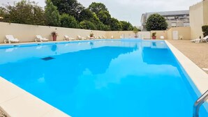 Ein rechteckiger Pool mit klarem, blauem Wasser, umgeben von weißen Liegestühlen und Topfpflanzen.