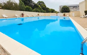 Ein rechteckiger Pool mit klarem, blauem Wasser, umgeben von weißen Liegestühlen und Topfpflanzen.