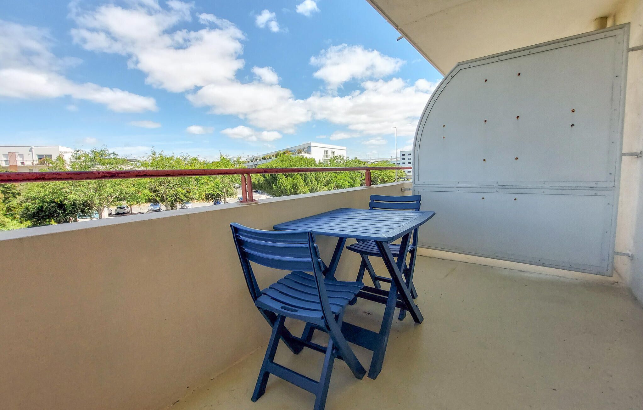 Un balcón con una mesa y sillas, vista del paisaje urbano y una puerta cerrada.