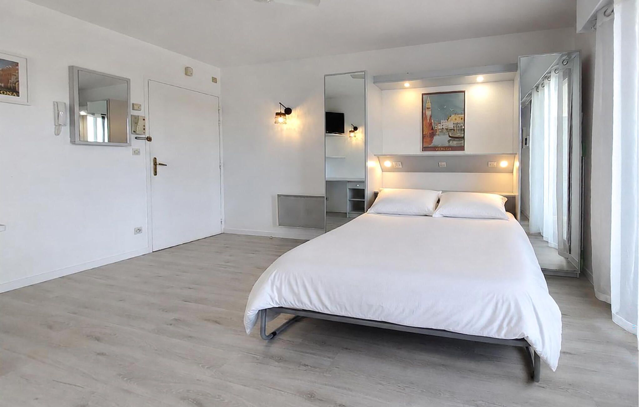 Moderni hotellihuone, jossa on suuri sänky, työpöytä, peili ja taulu seinällä.