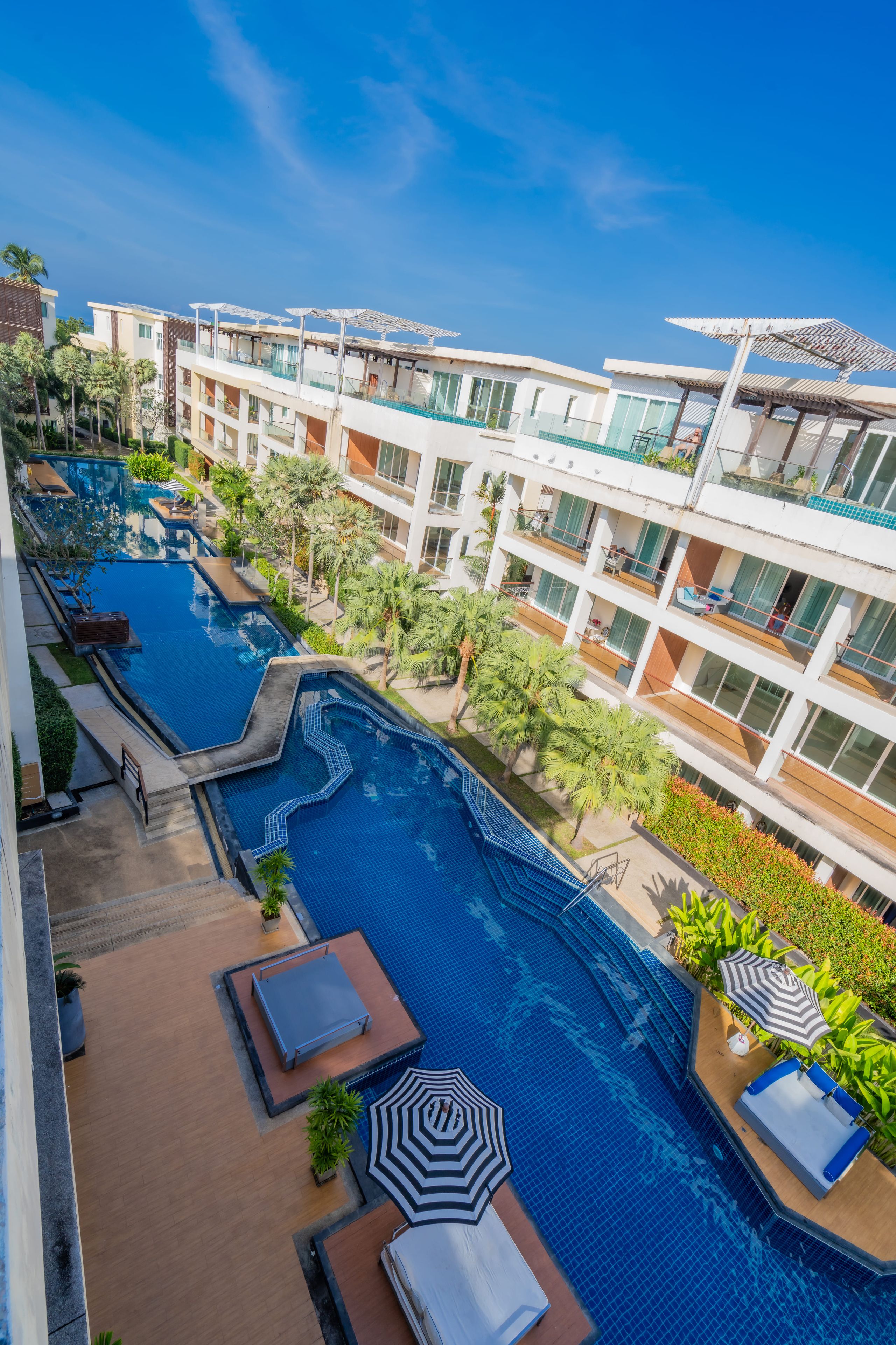 A multi-level hotel with a central swimming pool, outdoor seating, and lush landscaping.