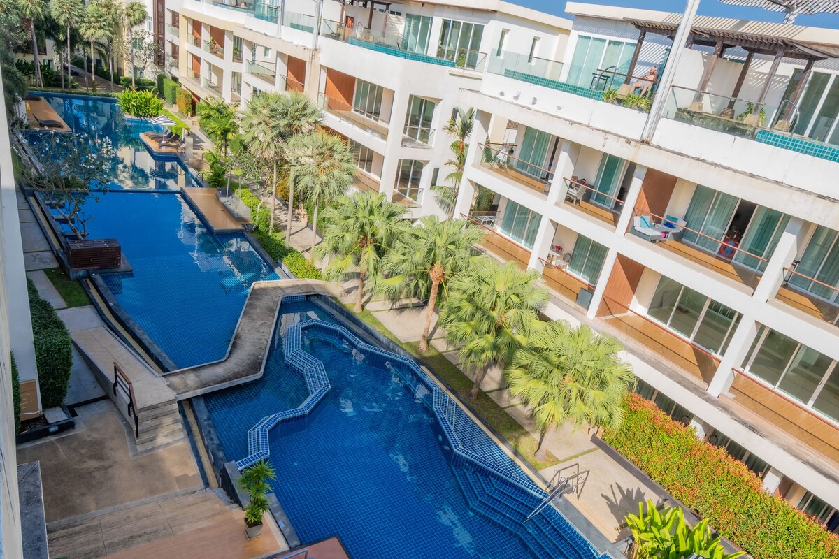 A multi-level hotel with a central swimming pool, outdoor seating, and lush landscaping.