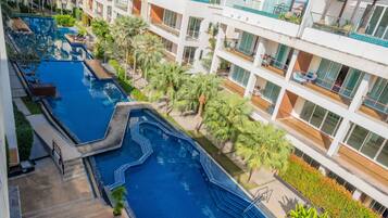 A multi-level hotel with a central swimming pool, outdoor seating, and lush landscaping.