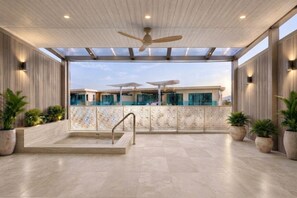 Un espacio interior amplio con piscina, ventilador de techo y plantas en macetas.