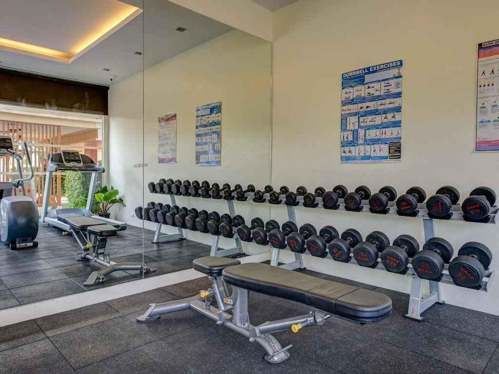 A gym with exercise equipment, dumbbells, and instructional posters on the wall.