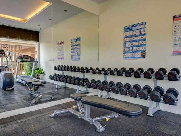 A gym with exercise equipment, dumbbells, and instructional posters on the wall.