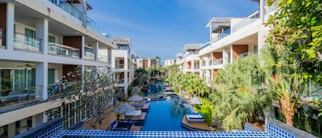 A modern hotel with a central swimming pool, multiple balconies, and lush greenery.