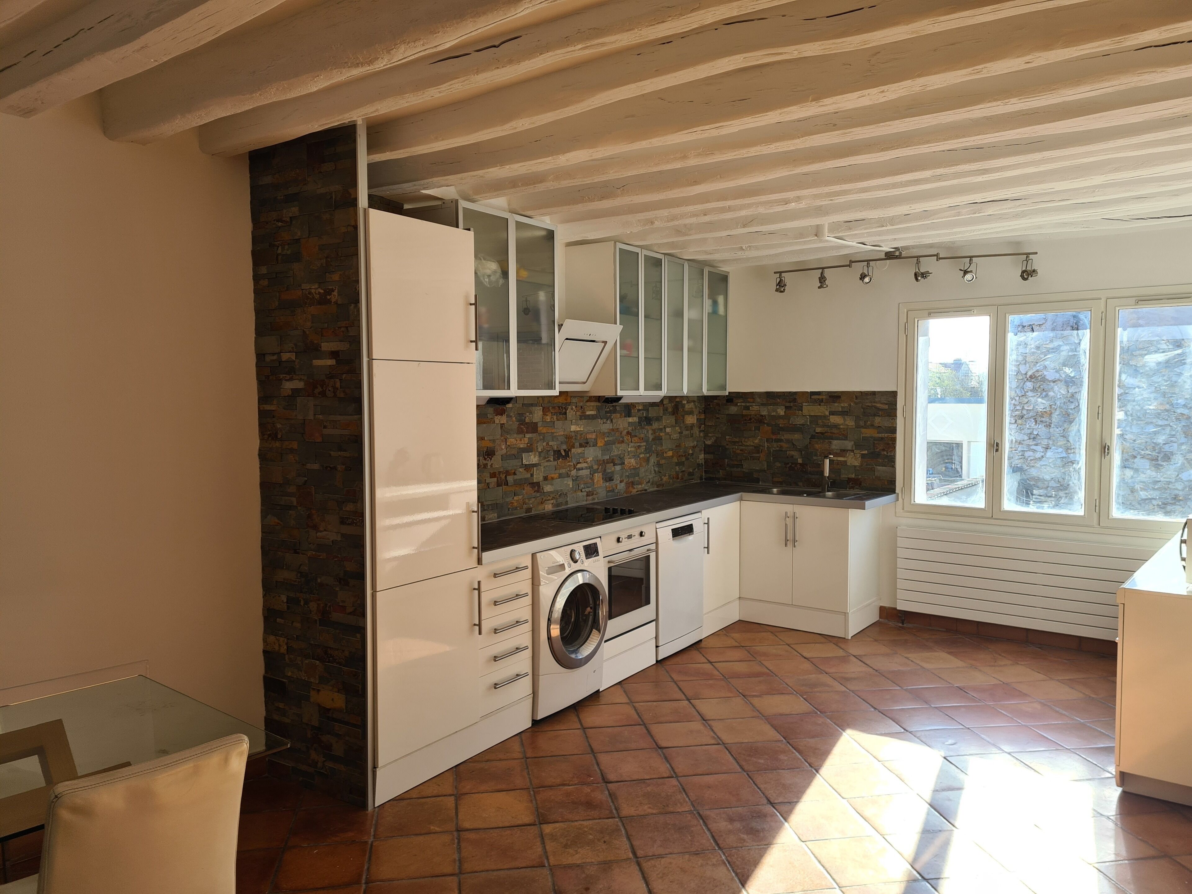 A kitchen with a stone backsplash, white cabinets, a washing machine, and a window with a view.
