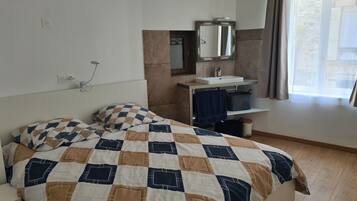 A hotel room with a bed, a bedside table, a mirror, a sink, and a window with curtains.
