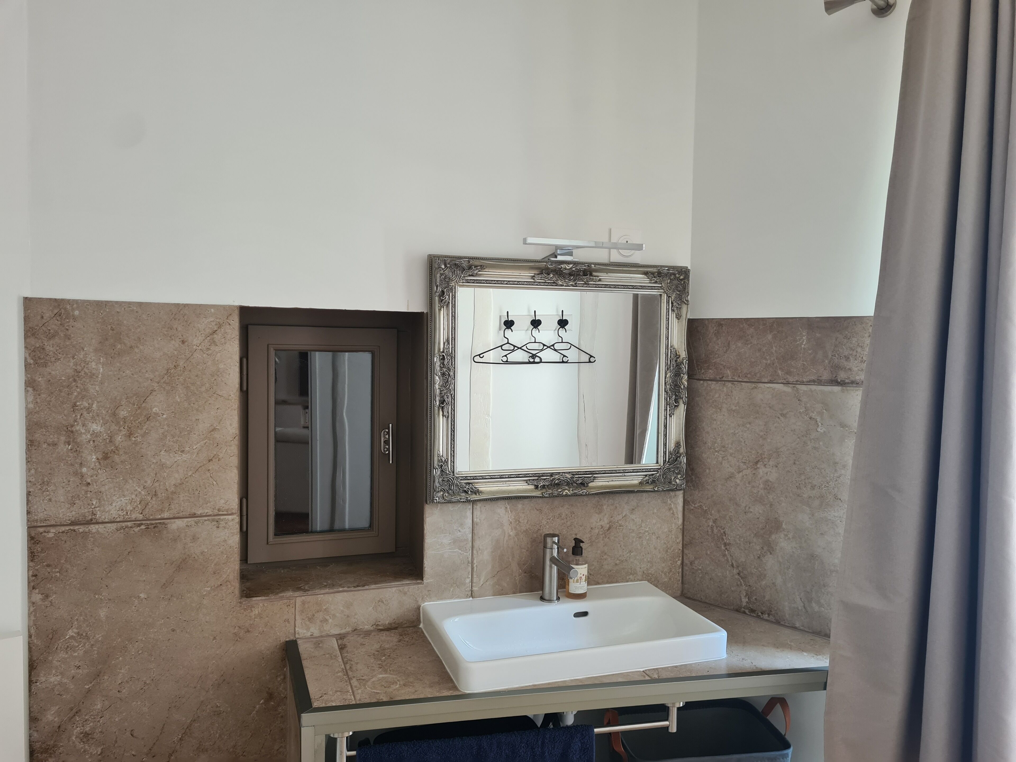 Une salle de bain avec un lavabo blanc, un miroir doté d’un cadre décoratif et un porte-serviettes.