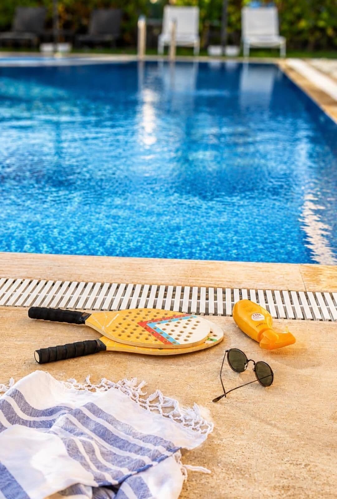 A poolside area with a paddleboard, sunscreen, sunglasses, and a striped towel.