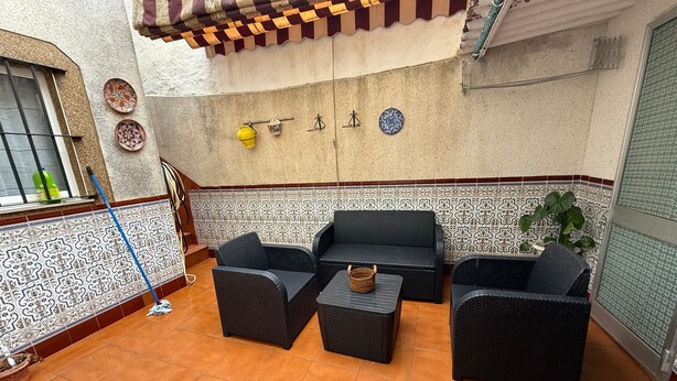 Ein Patio mit Korbmöbeln, gefliestem Boden und dekorativen Tellern an der Wand.