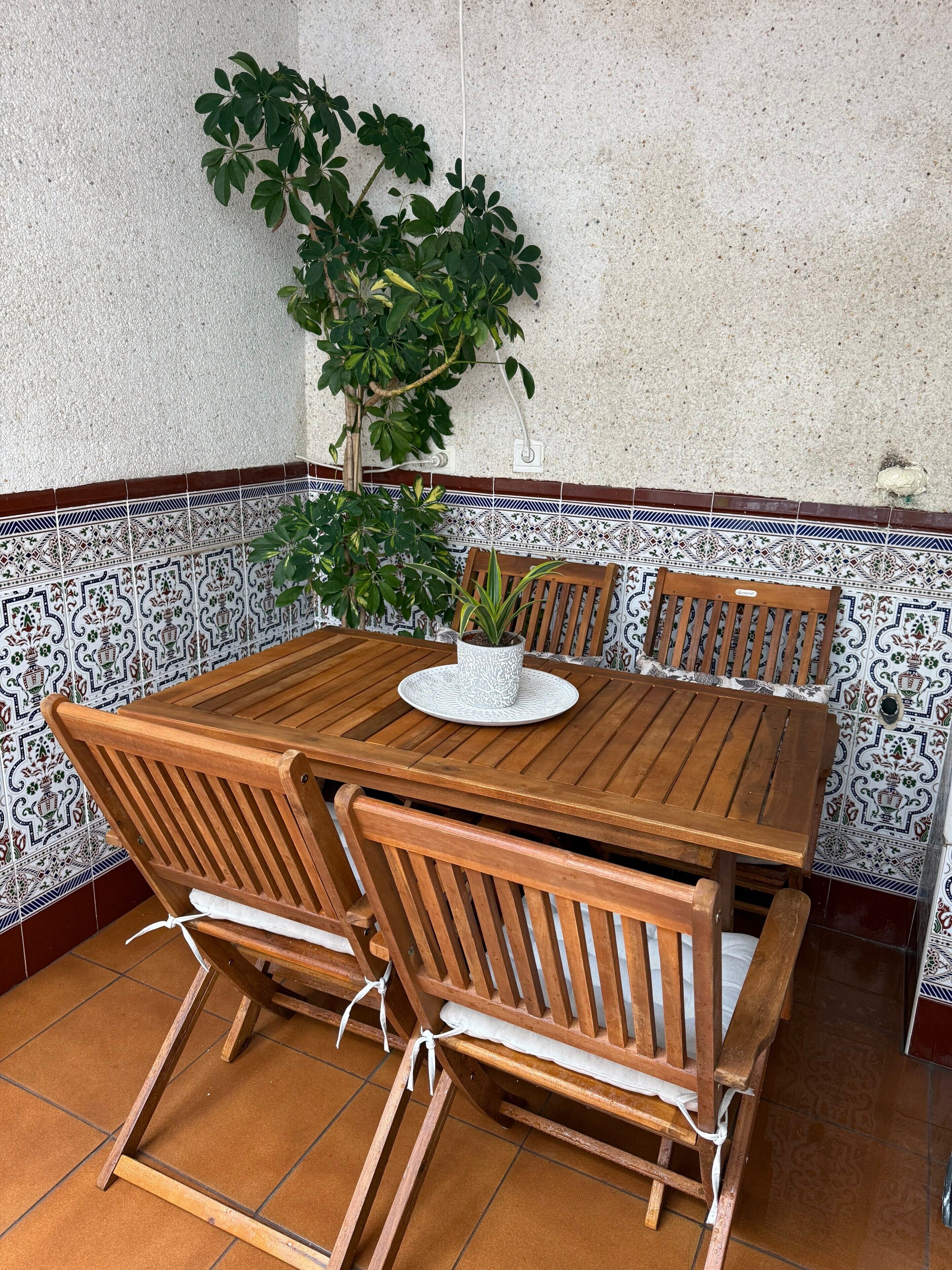 Een houten tafel met vier stoelen, een potplant en een betegelde muur met decoratieve rand.
