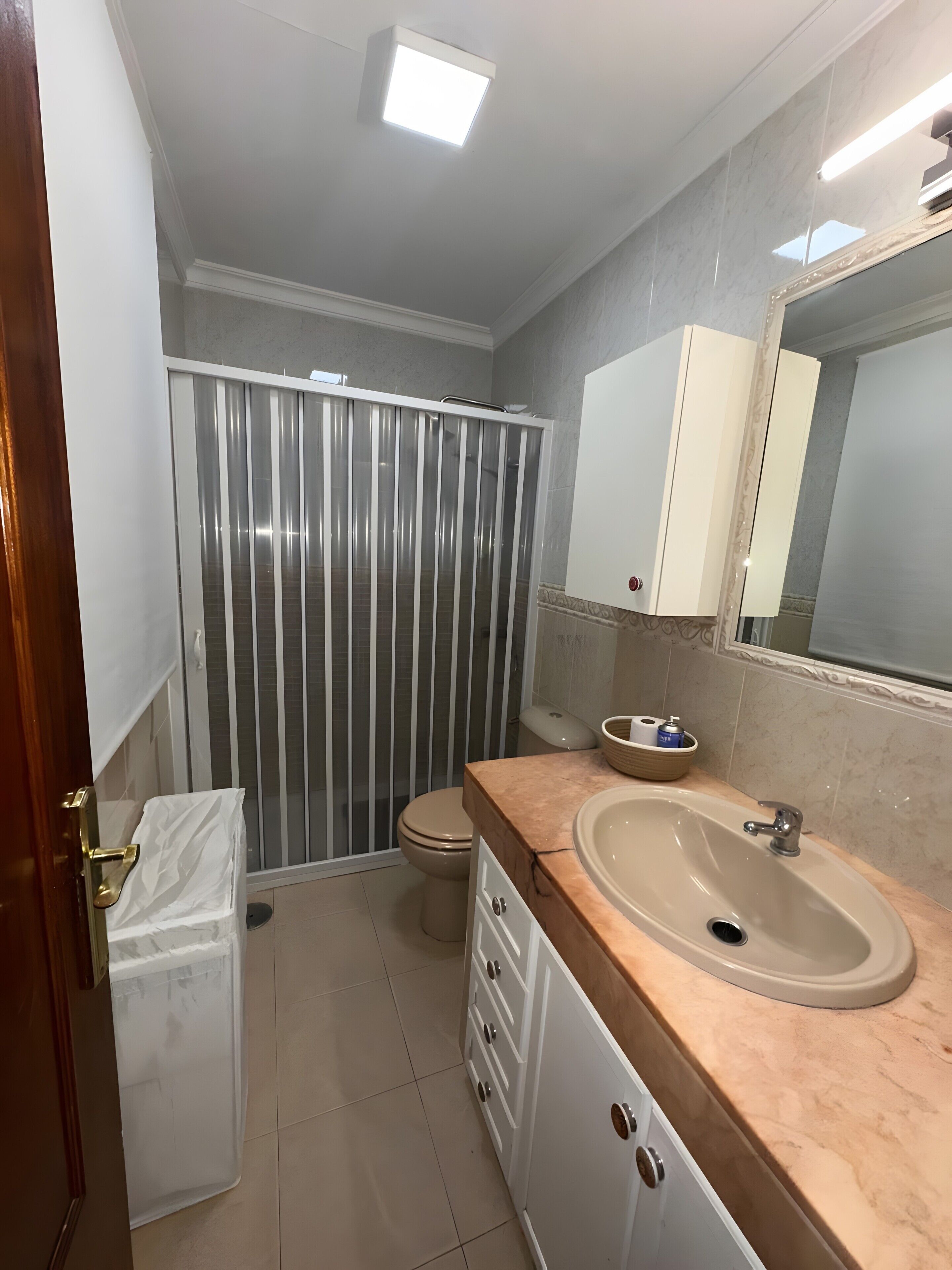 A bathroom with a toilet, sink, mirror, and a shower enclosure.