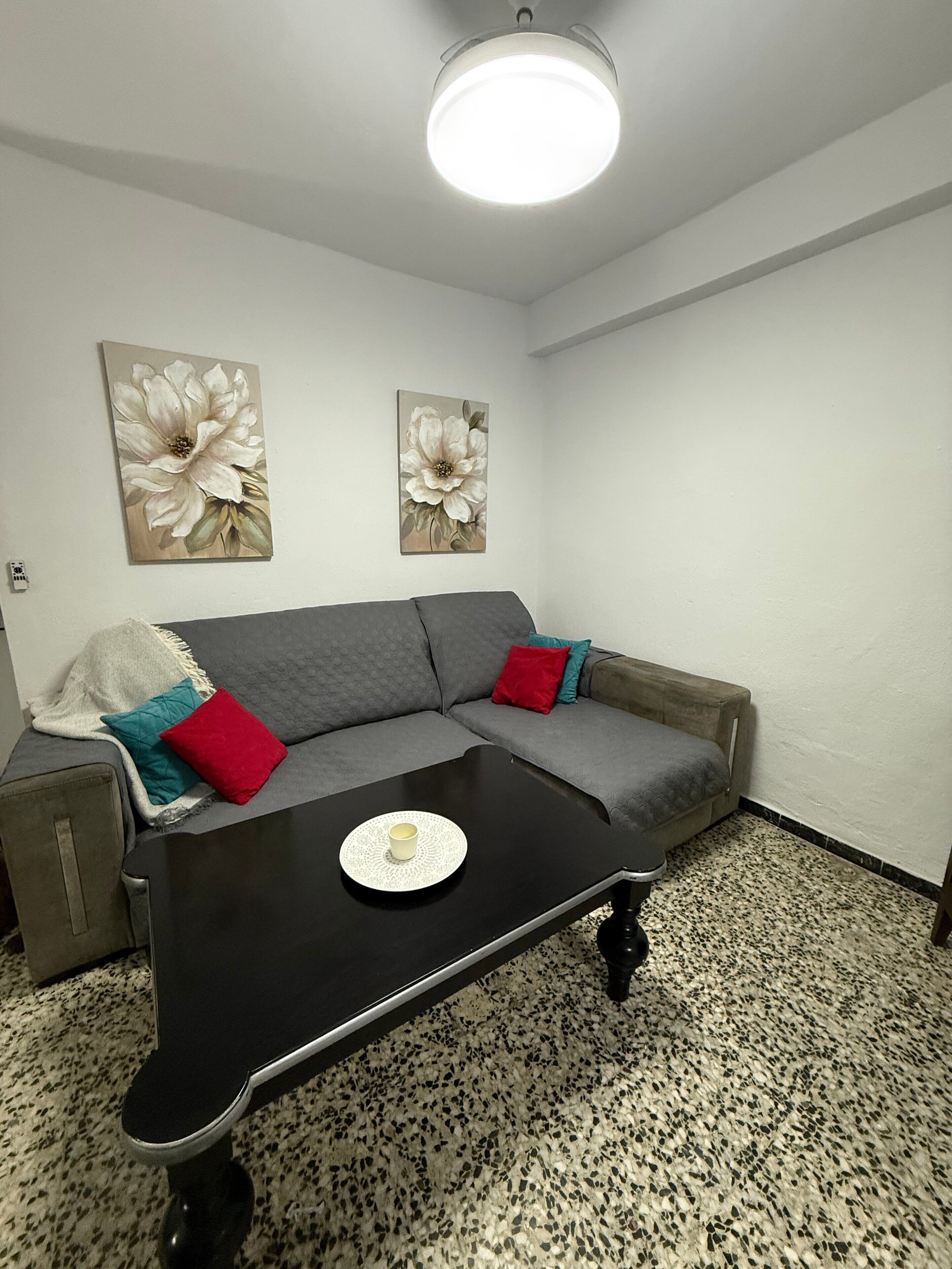 Una sala de estar moderna con un sofá seccional gris, una mesa de centro negra y dos cuadros florales en la pared.