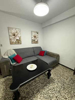 Ett modernt vardagsrum med en grå hörnsoffa, ett svart soffbord och två tavlor med blommotiv på väggen.