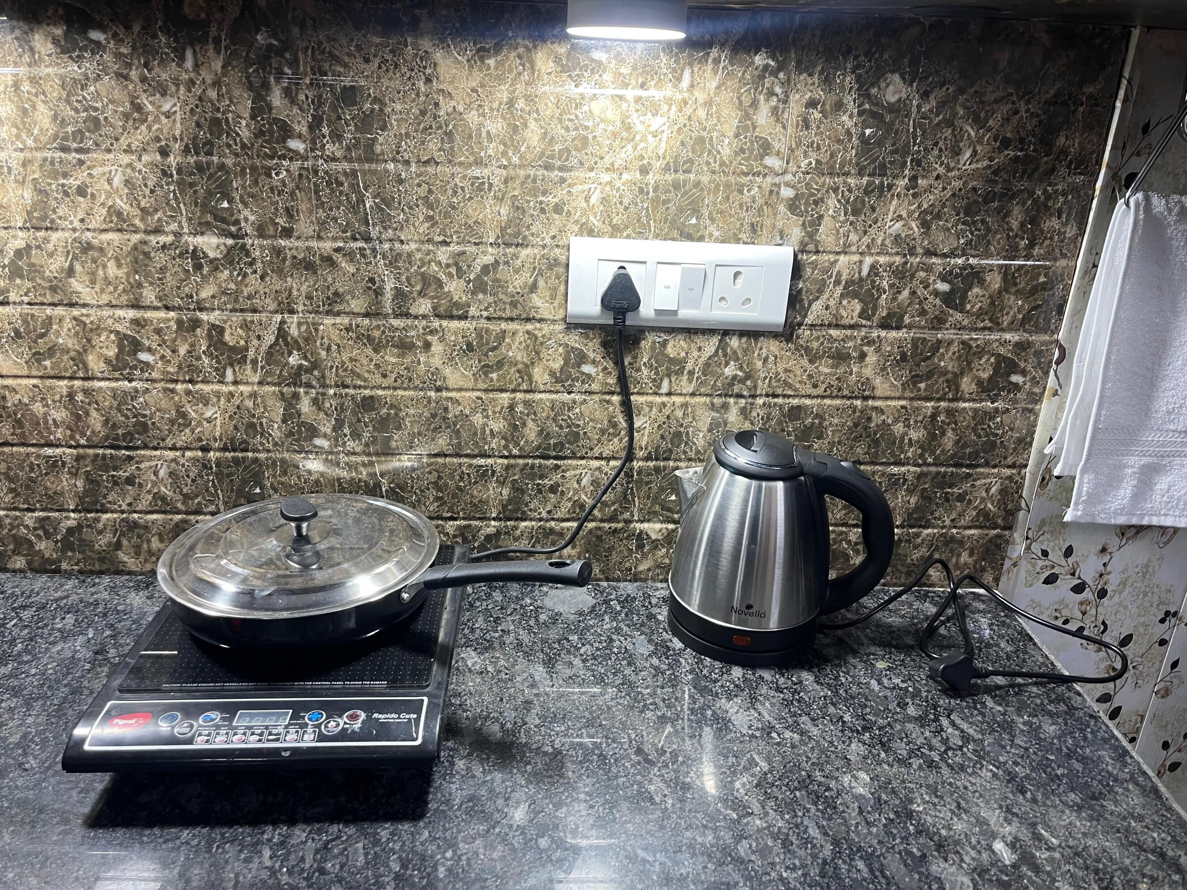 A kitchen with a scale, a kettle, and a wall socket.