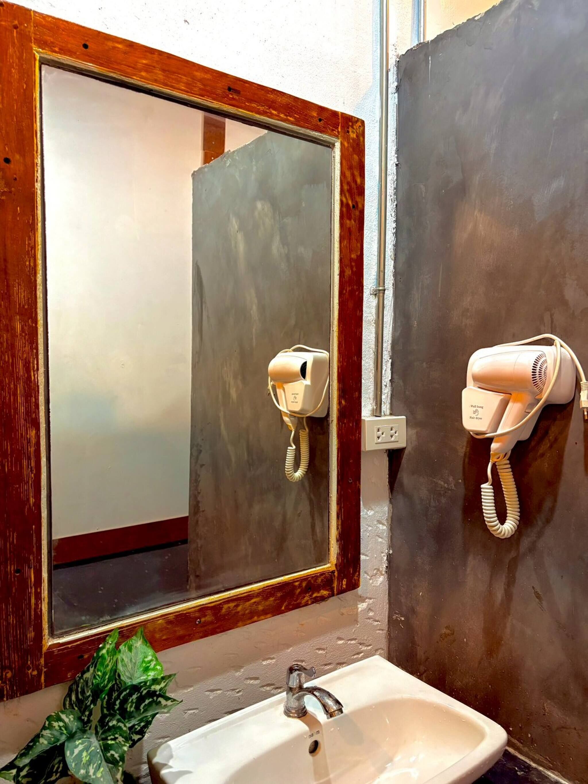 A bathroom with a mirror, a sink, and two hair dryers mounted on the wall.
