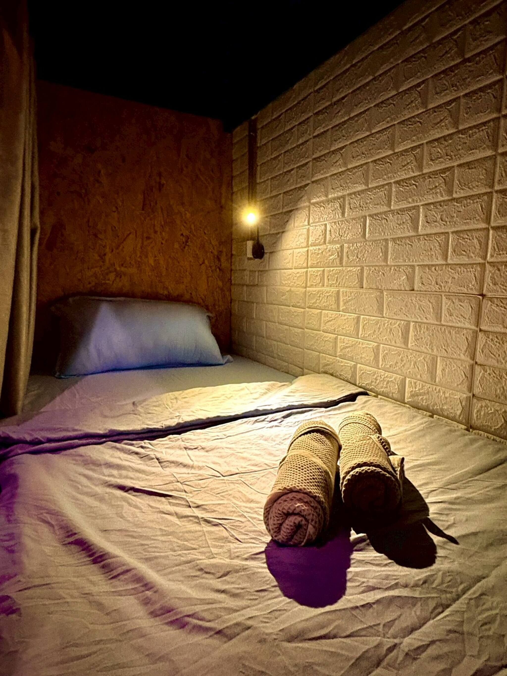 A single bed with a white headboard, a wall-mounted light, and a pair of shoes on the bed.