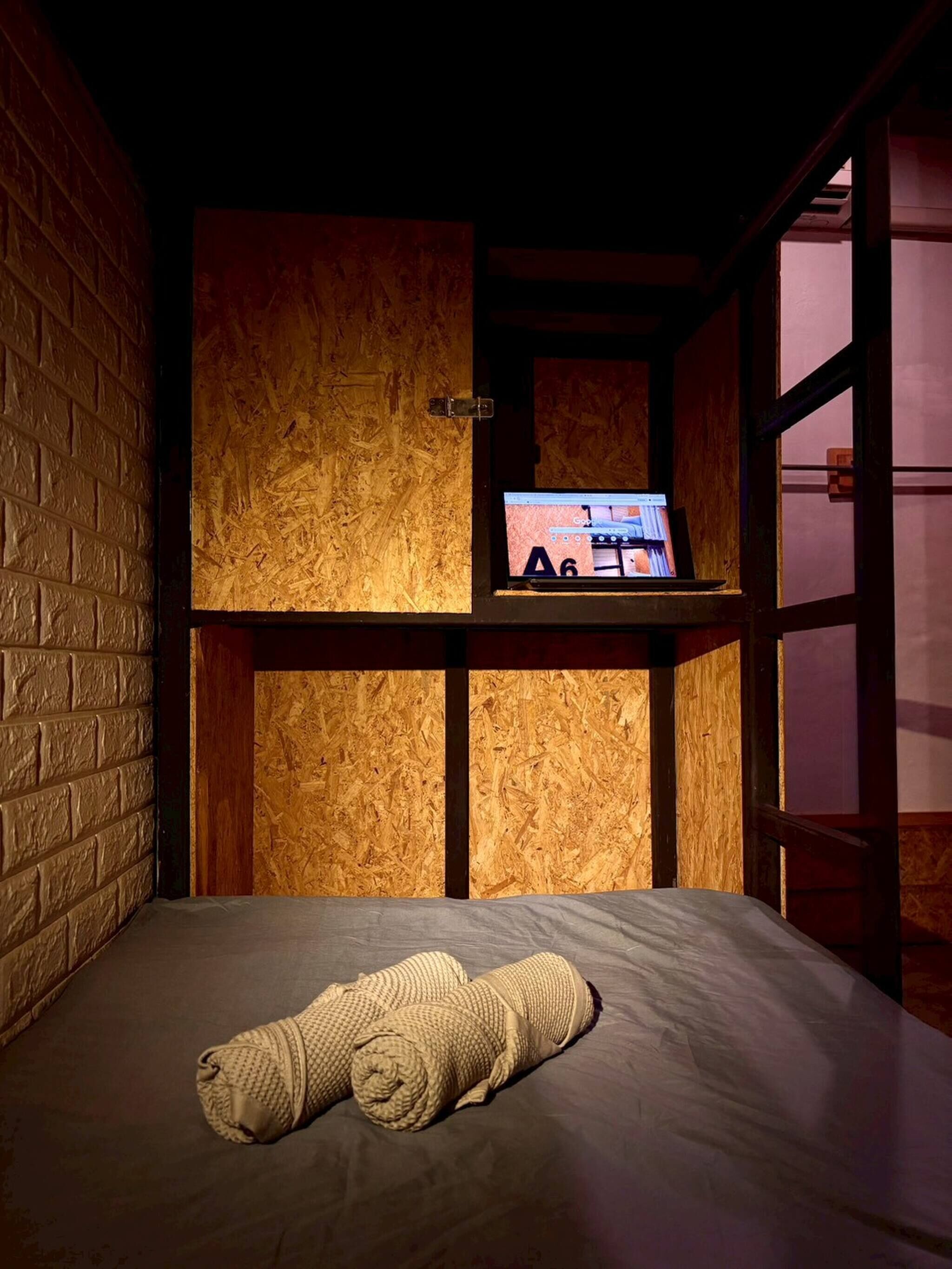 A room with a bunk bed, a laptop on a shelf, and a rolled-up blanket on the bed.