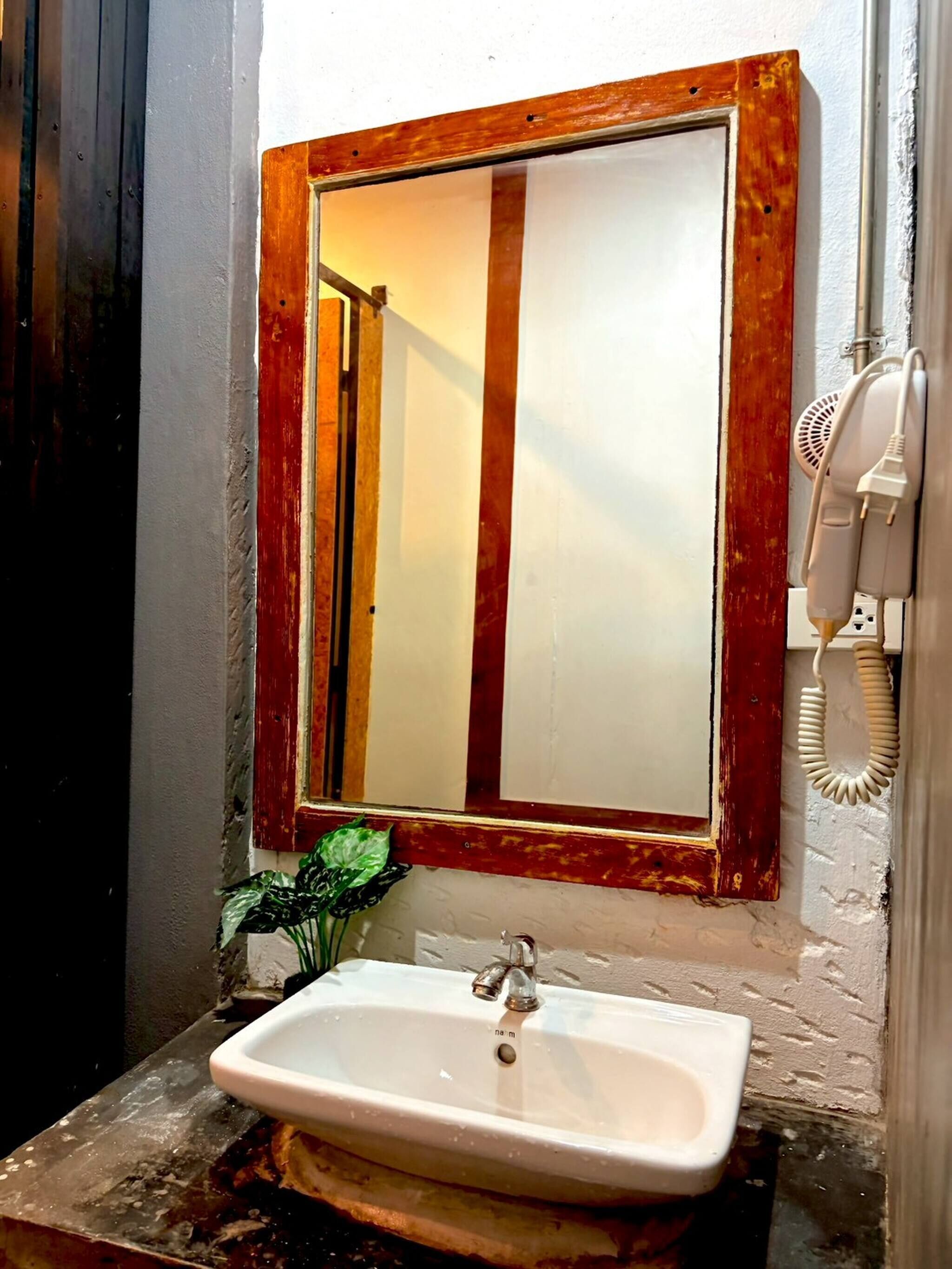 A bathroom with a white sink, a mirror with a wooden frame, and a hairdryer on the wall.