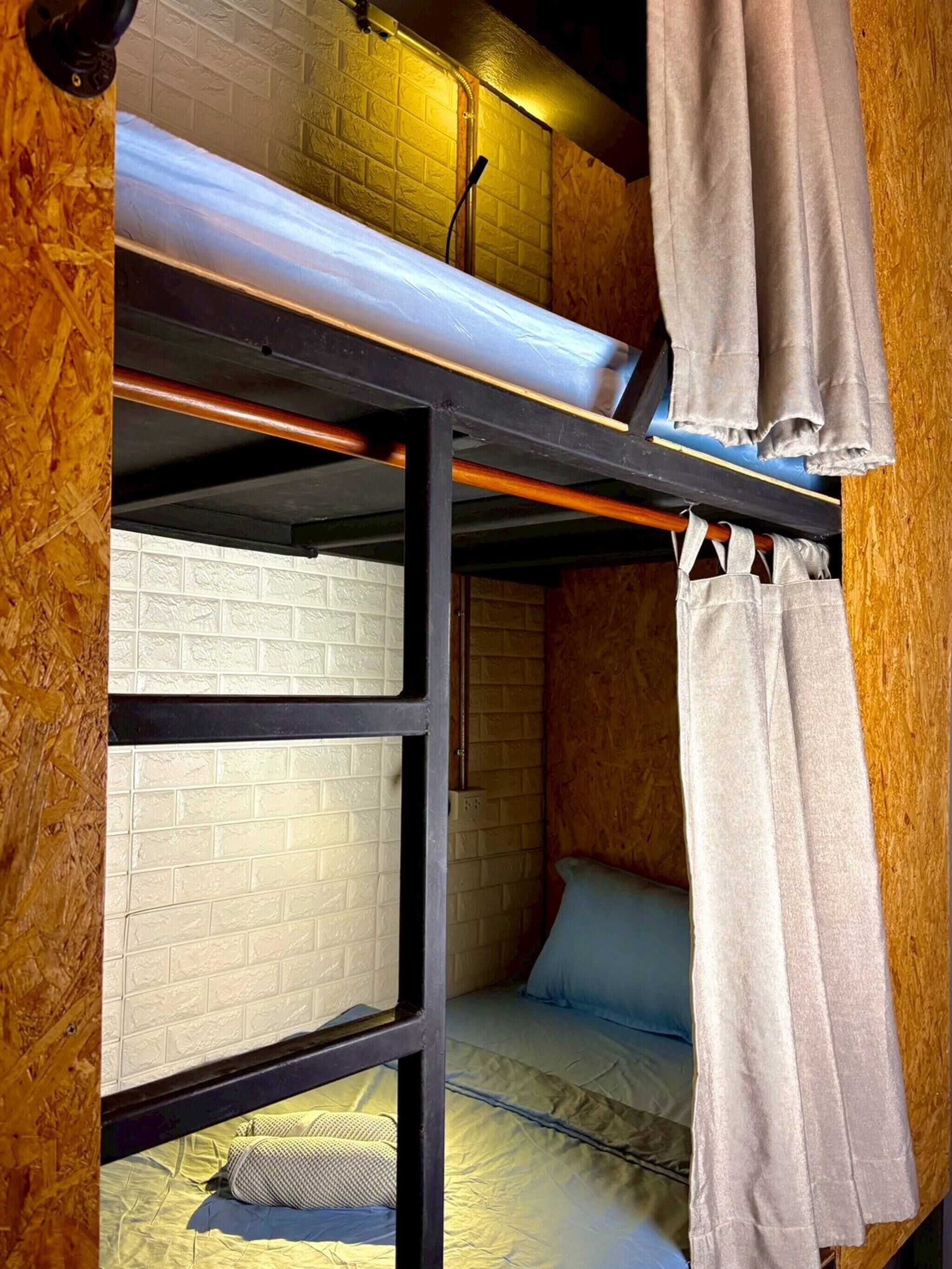 A bunk bed with a mattress on top and a lower bunk. There is a wooden wall with a textured pattern and a white brick wall.