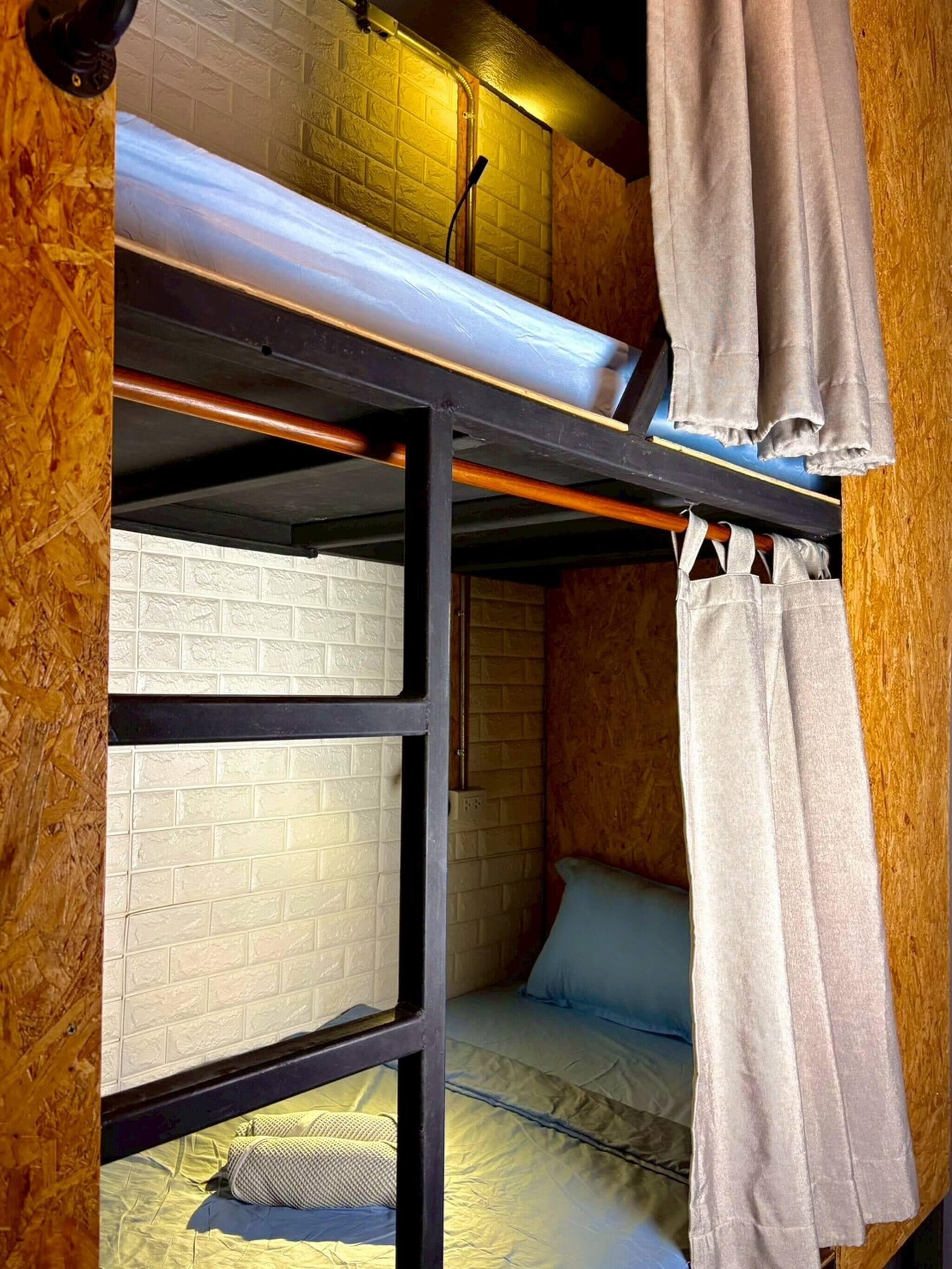 A bunk bed with a mattress on top and a lower bunk. There is a wooden wall with a textured pattern and a white brick wall.
