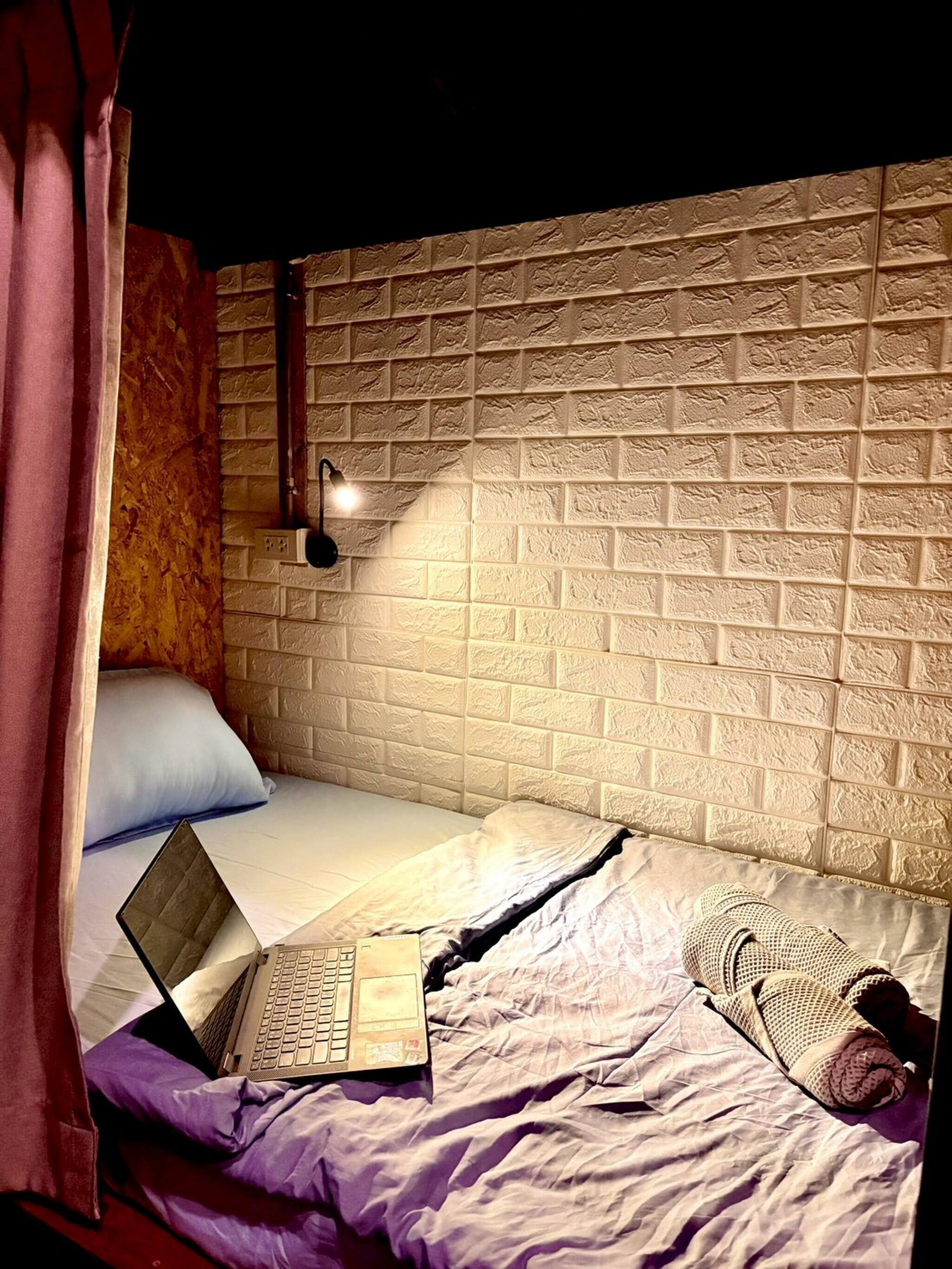 A single bed with a laptop, a lamp, and a blanket.
