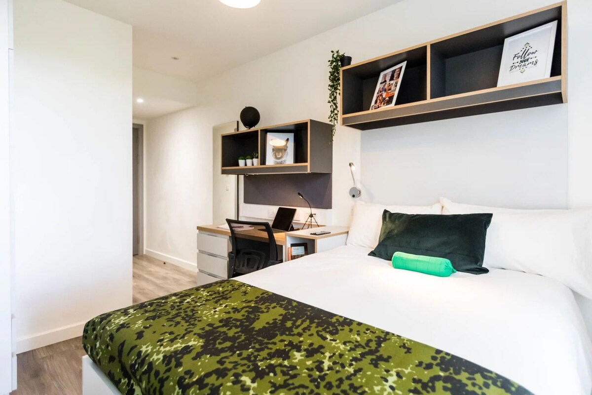 A bedroom with a bed, a desk, and a shelving unit.