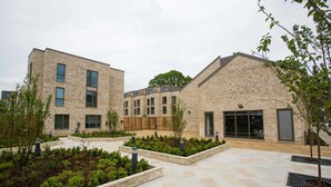 A modern building with a courtyard, featuring a mix of brick and glass facades, and surrounded by landscaped areas with trees and shrubs. - Student Only The Cam Foundry (Cambridge)