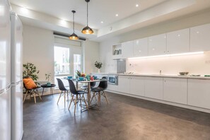 A modern kitchen with white cabinets, a dining area with black chairs, and a large window providing natural light. - Student Only The Cam Foundry (Cambridge)