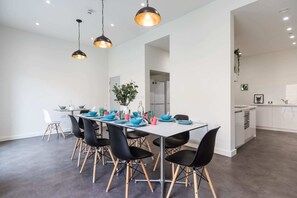 Ein moderner Essbereich mit einem langen Tisch, schwarzen Stühlen mit Holzbeinen und Pendelleuchten.