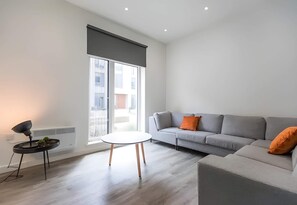 Ein modernes Wohnzimmer mit einem grauen Sofa, einem kleinen runden Tisch und einer Stehlampe.